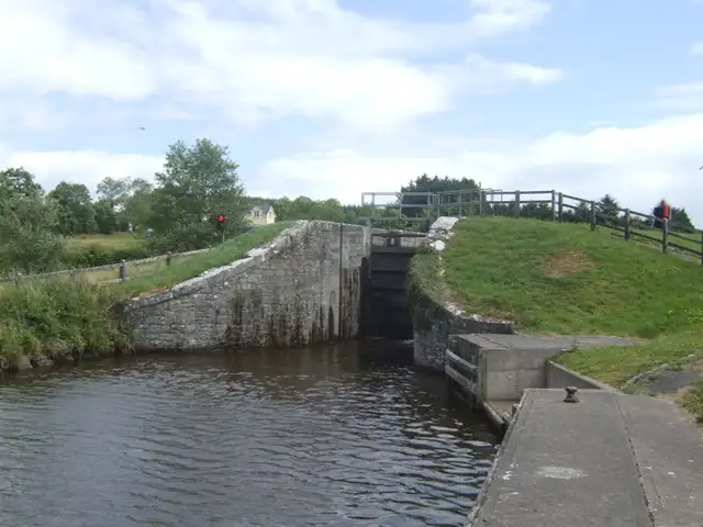 The tail of Kilclare Lower Lock (Lock 11) seen from the canal below, with stone wing walls, closed gates and grassy banks topped by a wooden fence.
