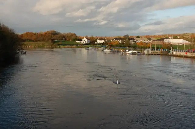 The Bann in flood at Portglenone, seen downstream from the bridge, with boats at the marina pontoons on the right and autumn trees and houses beyond.
