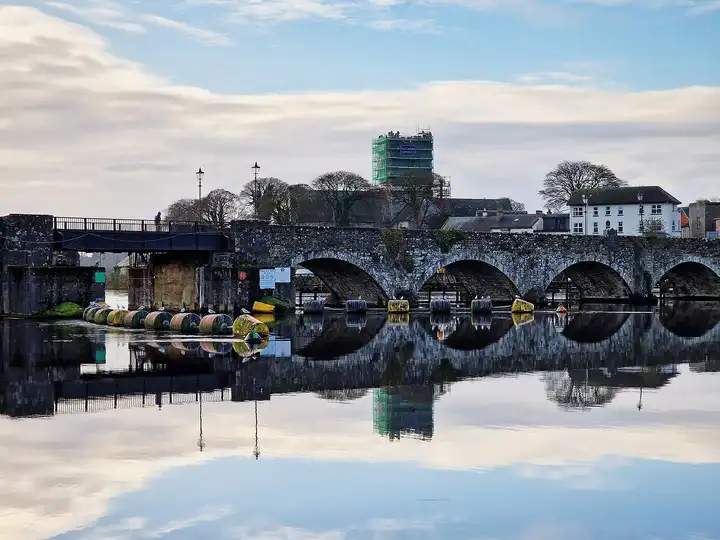 Le vieux pont de Killaloe et sa ligne de bouées se reflètent dans une eau lisse comme un miroir par un matin clair, avec derrière la tour échafaudée de la cathédrale Saint-Flannan.