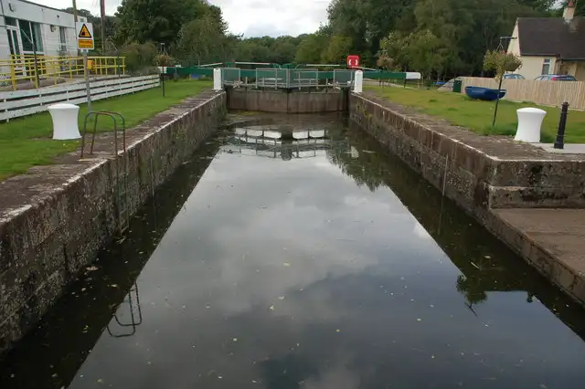 Die Steinkammer der Schleuse Movanagher spiegelt den Himmel, mit weißen Pollern, den hinteren Toren und einem Haus neben der Schleuse.