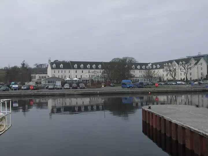 The harbour at Hodson Bay on a calm grey day, with a pier in the foreground and the long white Hodson Bay Hotel reflected in the water.