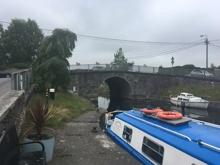 Sallins Bridge seen from the quay, with a blue-and-white trip barge moored in the foreground and a small cruiser tied up beyond.