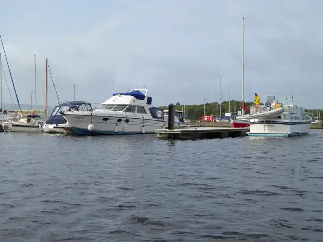 Motor cruisers and sailing boats moored at a floating jetty in Mountshannon Harbour, seen from the water on an overcast day.