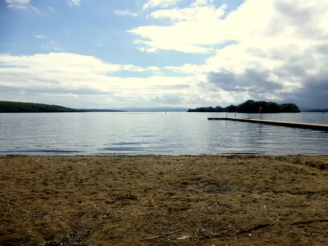 Ein langer Holzsteg führt von einem Sandstrand am Lower Lough Erne bei Kesh in den See, am Horizont bewaldete Inseln.