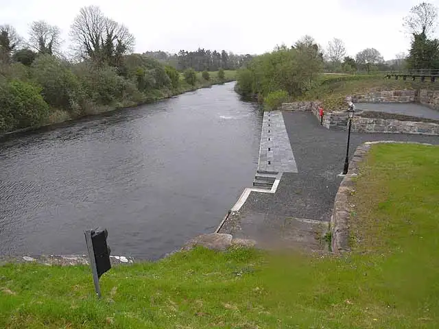 The broad channel below Castlefore Lock, with the paved lock landing, a lamp post and low stone walls beside the grassy bank.