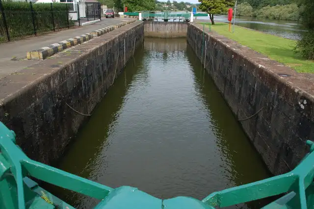 Looking from a green gate beam along the long stone chamber of the lock at the Cutts, with the River Bann and wooded banks beyond.