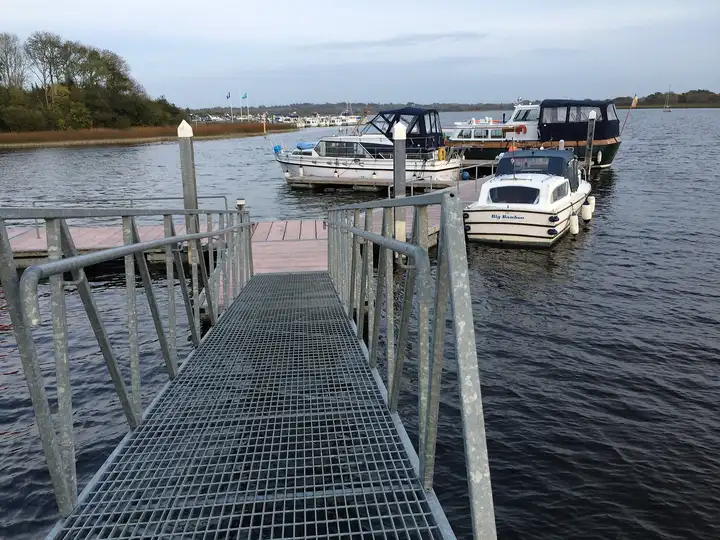 Motorkreuzer am Schwimmsteg von Coosan Point, gesehen von der Gangway, gegenüber auf dem Wasser eine Marina mit Flaggen.
