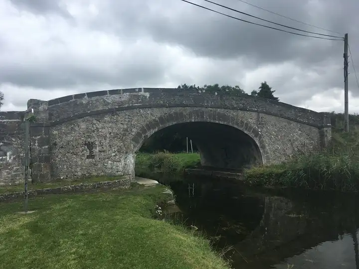 Bond Bridge near Allenwood, a broad stone arch over the canal, with a grassy towpath in front under a cloudy sky.