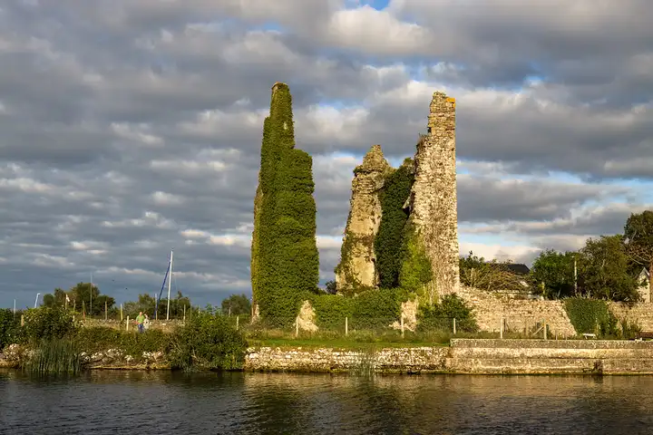 Die efeubewachsene Ruine der Burg von Dromineer, gesehen über das ruhige Wasser des Hafens.
