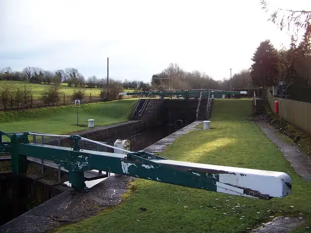 A green balance beam of the lock gates at Portna in the foreground, with the lock chamber, a grassy bank and bare winter trees behind.
