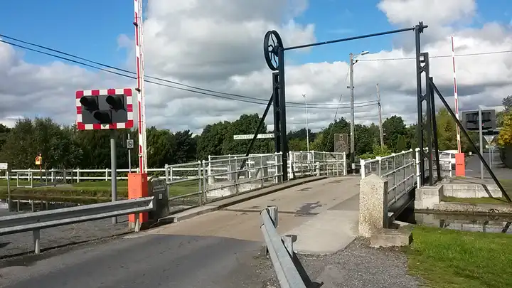 The road deck of the Monasterevin lifting bridge on the R424, with its overhead wheel, traffic lights and red-and-white barriers.