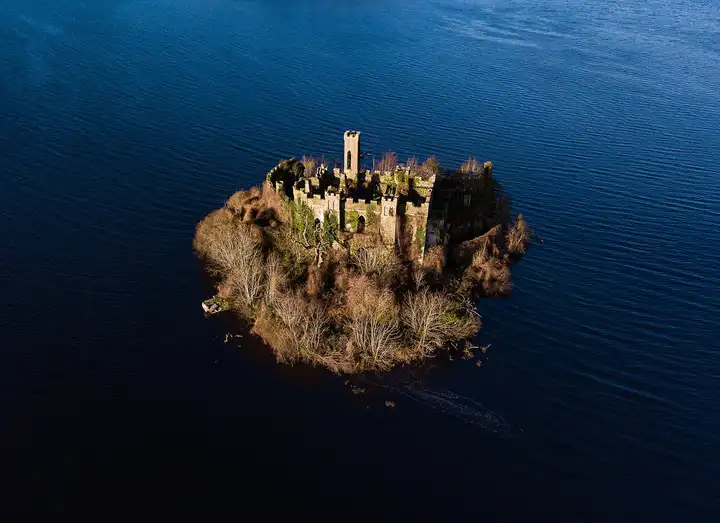An aerial view of Castle Island, its ruined castle and bare winter trees rising from the deep blue water of Lough Key.