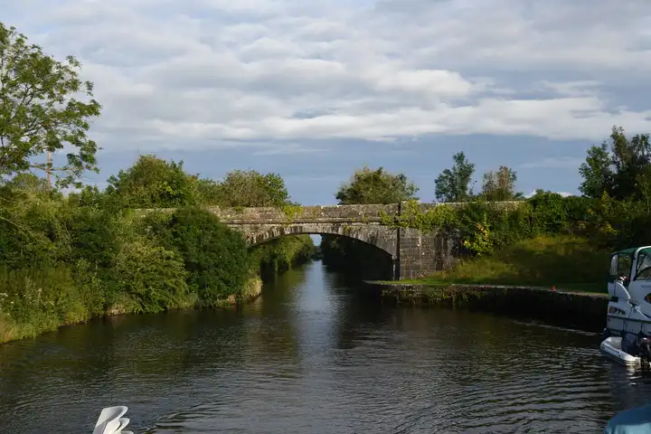Seen from a cruiser in evening light, a single-arch stone bridge crosses the Jamestown Canal near Jamestown, with a moored boat on the right.