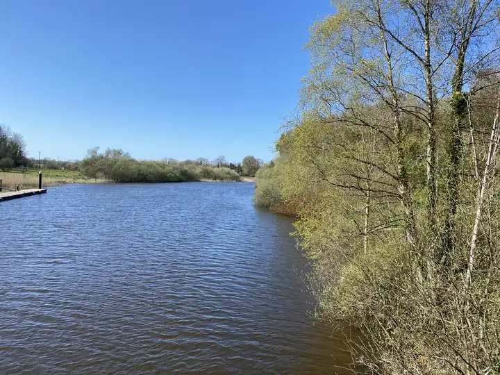 The River Erne channel beside Belle Isle under a clear blue sky, with a small jetty on the left bank and birch trees on the right.