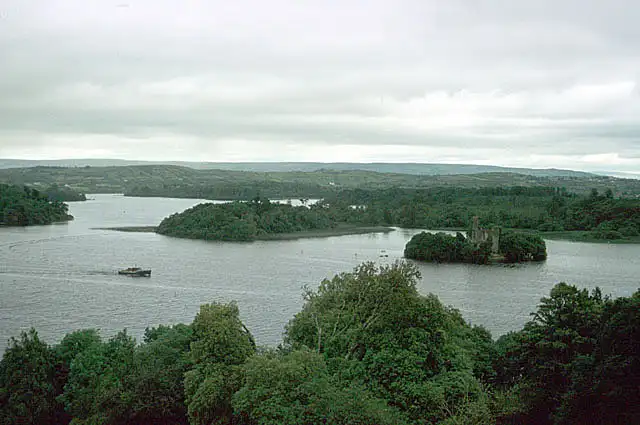 Beboste eilanden, waaronder Castle Island, verspreid over Lough Key, van hoog boven het bospark gezien, met één boot op het water.