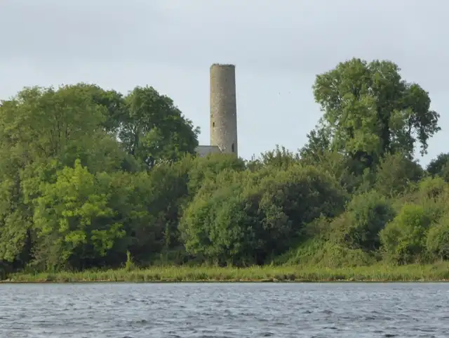 Der Rundturm von Inis Cealtra ragt über die Bäume der Insel, vom Wasser aus gesehen.
