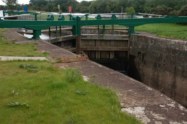 Die grünen Schwenkbalken und geschlossenen Holztore an einem Ende der Schleuse Carnroe, vom grasbewachsenen Schleusenrand aus gesehen.