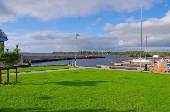 Eine Rasenfläche am Hafen von Dromineer mit Blick über die Stege und die Hafenmauer auf den offenen See.