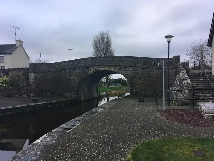 The stone arch of Richmond Bridge spans the canal at the harbour in Clondra on an overcast winter day, with a paved quay, a lamp post and steps on the right.