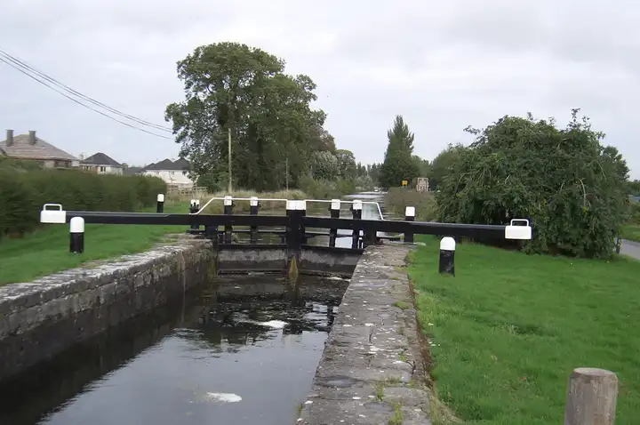 The stone chamber of Lock 23 at Rathangan with its black-and-white balance beams, grassy banks and houses beyond.
