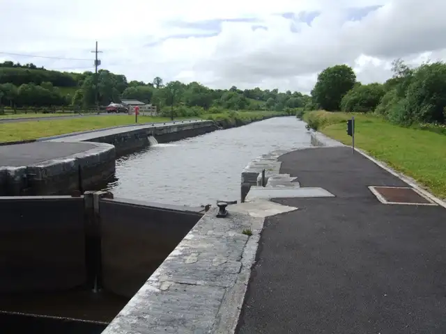 Castlefore Lock (Lock 8) seen from its gates, with the stone-edged canal stretching away between a tarmac lockside path and green fields.