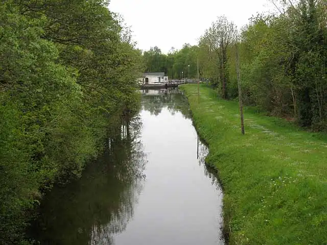 The narrow Lough Allen Canal runs straight between a grassy towpath and trees towards a white building in the distance.
