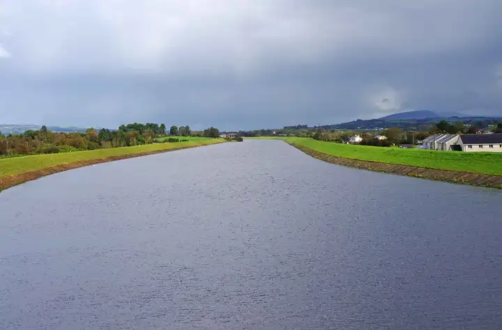The wide, straight headrace canal runs between grassy embankments near O’Briensbridge under a grey sky.