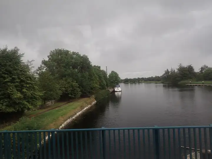 Seen from the N5 bridge on an overcast day, the Shannon at Tarmonbarry runs between tree-lined banks, with a cruiser moored on the left and a floating jetty on the right.