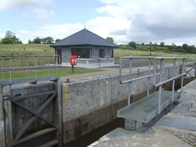 Killarcan Lock (Lock 16) on the Shannon–Erne Waterway, with its stone chamber, a steel walkway over the gates and a small slate-roofed stone hut beside the lockside path.