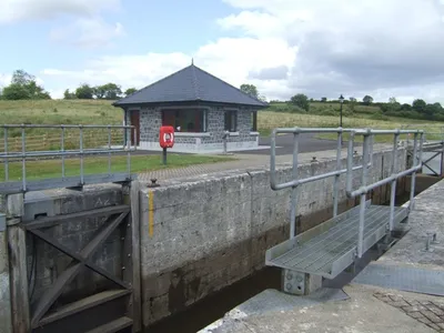 Killarcan Lock (Lock 16) on the Shannon–Erne Waterway, with its stone chamber, a steel walkway over the gates and a small slate-roofed stone hut beside the lockside path.