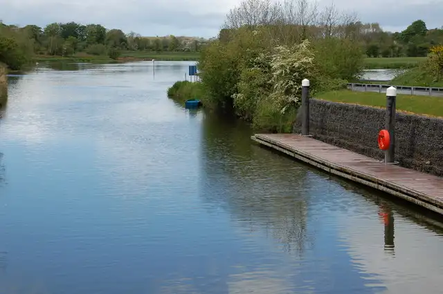 The calm navigation channel below the locks at Portna, with a waiting pontoon, a lifebuoy and bollards on the right and the river visible beyond the trees.