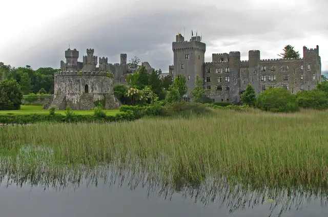 Die Türme und Zinnen von Ashford Castle bei Cong, gesehen über Schilfgürtel und stilles Wasser am Rand des Lough Corrib.