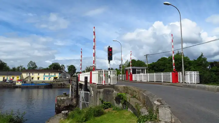 The road across Roosky Bridge passes the lifting span with its red-and-white barrier poles and traffic light, with boats and the village quay across the water on the left.