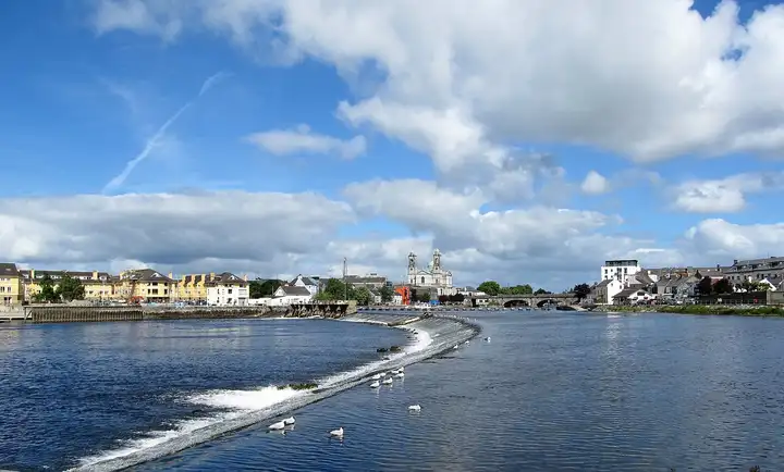 The curved weir across the Shannon at Athlone, with gulls on its sill and the town’s quays, bridge and twin-towered church beyond.