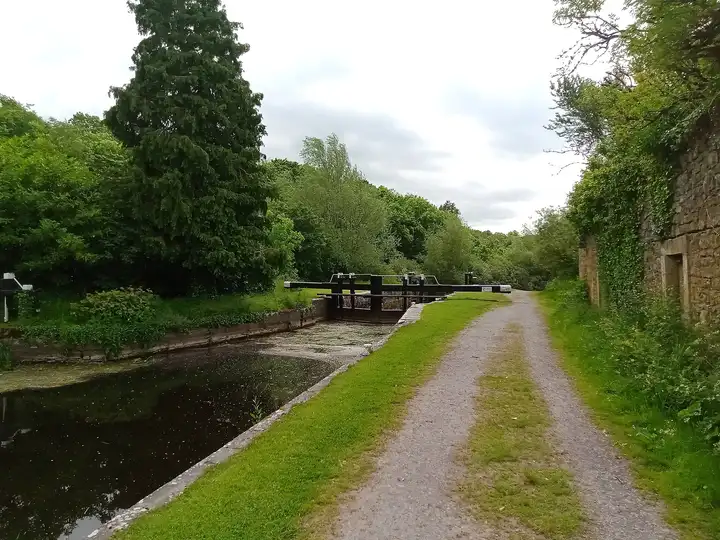 The gravel towpath beside Milford Lock, with the lock gates ahead, tall trees and an old stone wall on the right.