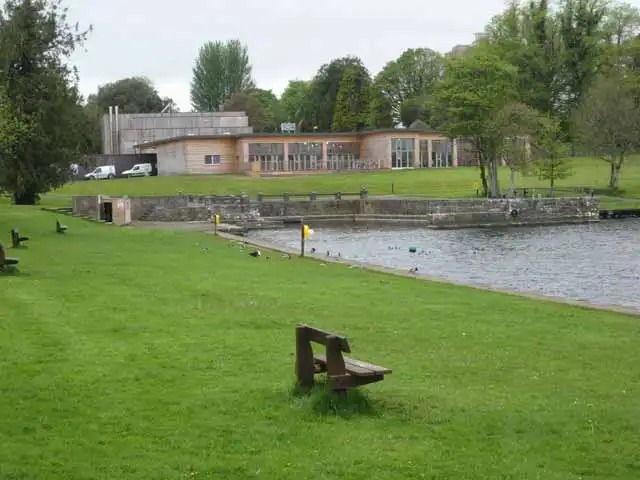 Het bezoekerscentrum van Lough Key Forest Park staat boven de havenmuur, met een houten bank op het gazon ervoor.
