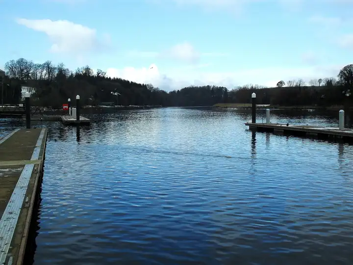 Leere Schwimmstege am Round O Quay in Enniskillen ragen in den ruhigen, blauen River Erne, mit Blick nach Norden auf bewaldete Ufer.