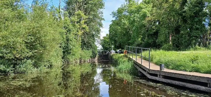 La dérivation verdoyante de Levitstown menant aux portes de l’écluse, avec un ponton d’attente en bois et une bouée de sauvetage sur la rive droite.