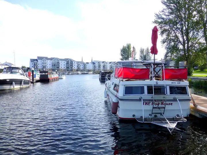 Motor cruisers and a canal boat moored at the Round O pontoons in Enniskillen, with white apartment blocks and two church spires across the River Erne.