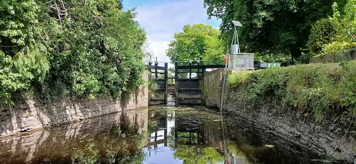 Vue depuis l’eau le long du sas en pierre de l’écluse de Levitstown vers ses portes, encadrée par des arbres en surplomb.