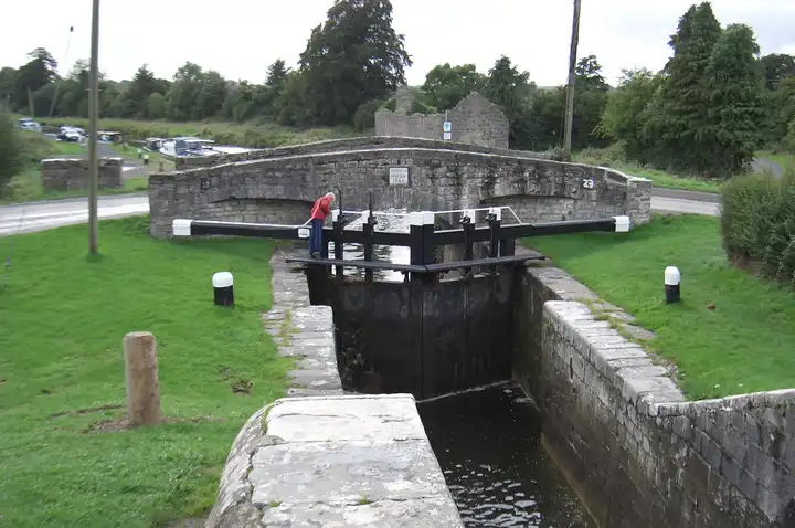 Lock 23 on the Barrow Line at Rathangan, its black-and-white gates below the stone arch of Spencer Bridge, with boats moored along the canal beyond.