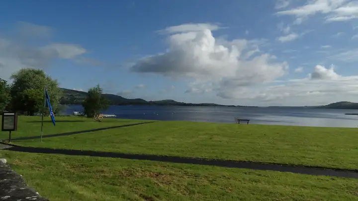 The lakeside lawn at Ballycuggaran, with a bench at the water's edge and Lough Derg stretching away under a bright sky.