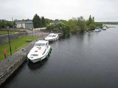Two white hire cruisers lie along the stone quay at Cootehall, seen from above, with the River Boyle widening towards Cootehall Lough.