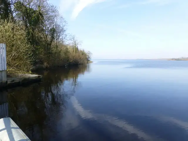 From the jetty at Muckross, glassy water mirrors the wooded bank and a pale blue sky that stretches out over the open lough.
