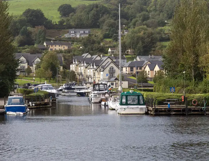 Bateaux de croisière et un voilier amarrés dans la marina de Harbour Village à Killaloe, avec des immeubles d'appartements et des collines vertes à l'arrière-plan.