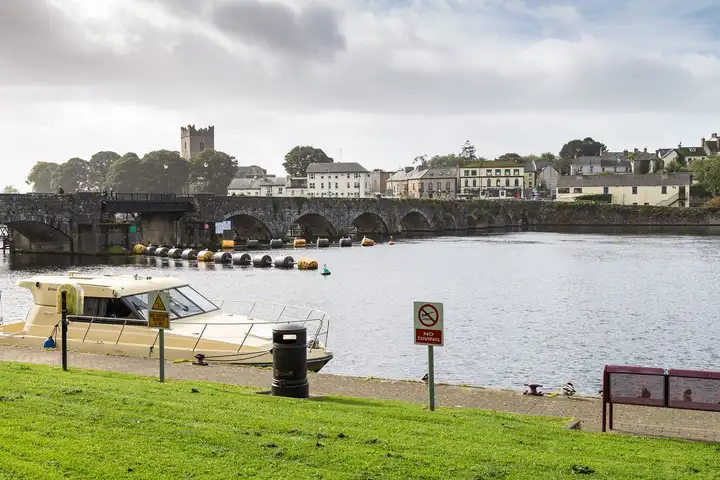 A cruiser moored at the Ballina quay, looking across the Shannon to the old stone bridge, the tower of St Flannan's Cathedral and the houses of Killaloe.