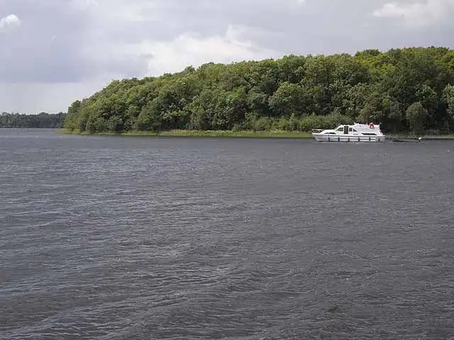 A white cruiser off the wooded shore at the eastern end of Garadice Lough, under a grey sky.