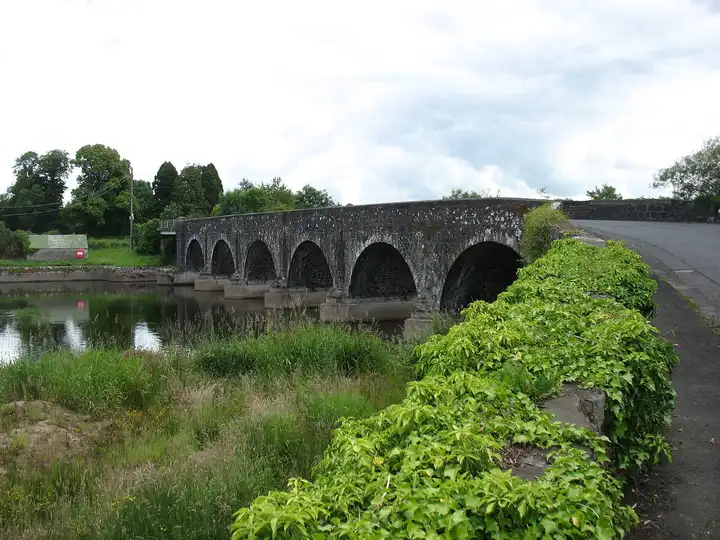 Kilrea Bridge, a long stone bridge of several arches, crosses the Bann between green banks, with ivy along the parapet in the foreground.