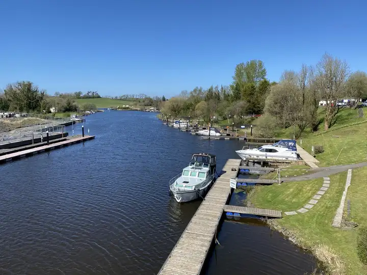 Motor cruisers moored at the wooden jetties of Carrybridge marina on a channel of the River Erne, seen from above on a sunny spring day.