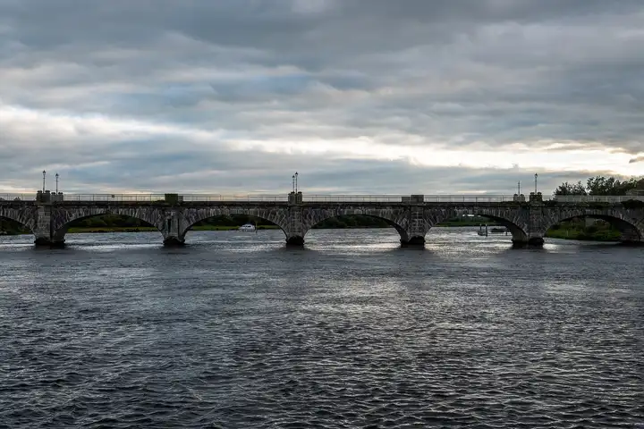 Banagher Bridge seen side-on across the Shannon on an overcast evening, its low arches spanning the whole width of the river.